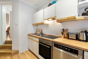 A modern kitchen with white cabinets, a wooden countertop, stainless steel appliances, and a visible staircase leading to another room. - Stylish Apartment in Prime Location with Wi-Fi (Nürnberg)