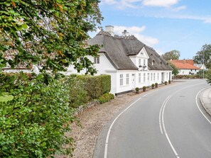 A white building with a thatched roof, a curved road, and a hedge in the foreground. - 5 Star Holiday Home in Millinge (Millinge)