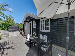 A wooden house with a patio area featuring a table and chairs, a large umbrella, and a view of the surrounding greenery. - 4 Star Holiday Home in Allinge (Allinge)