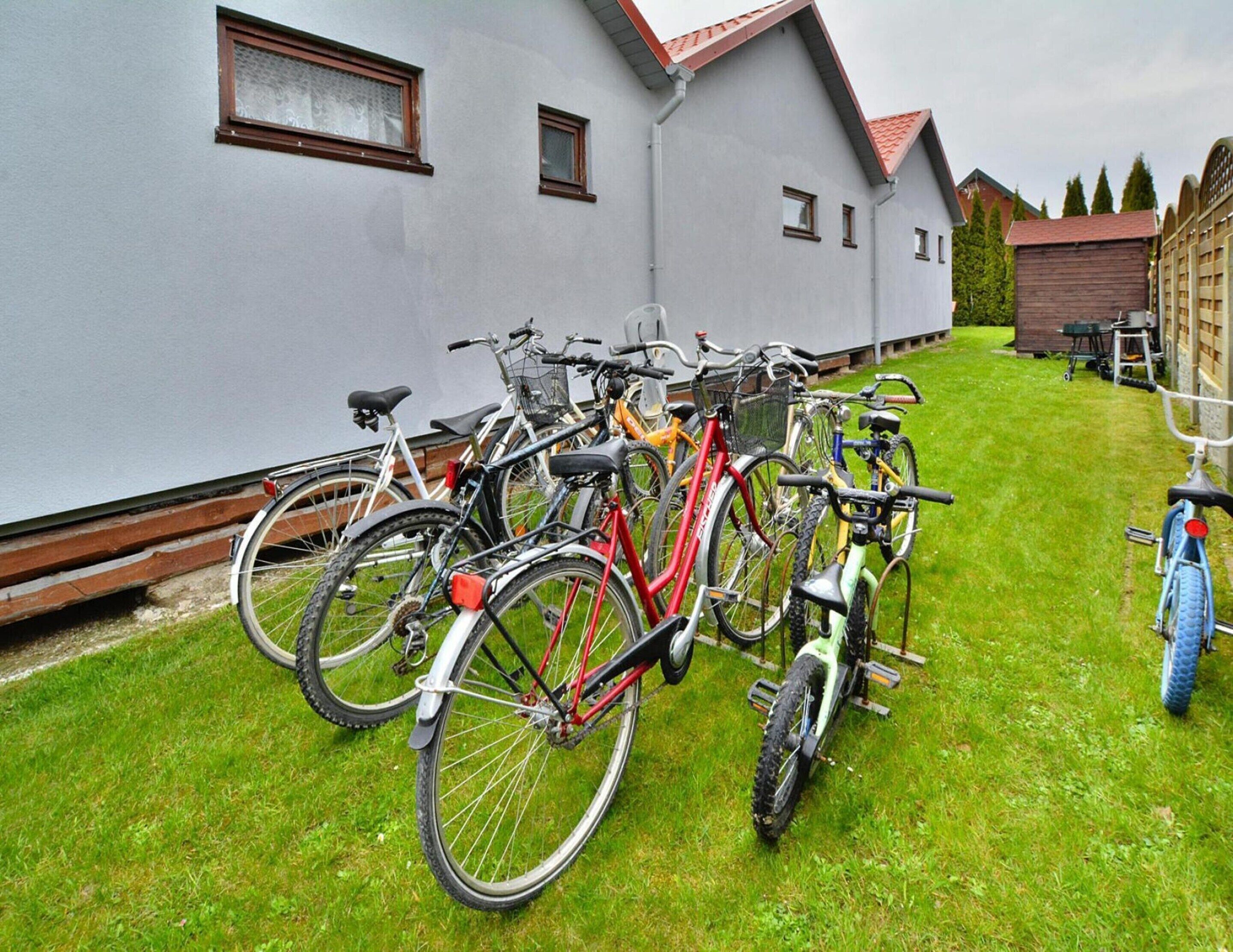 Bicycles parked in a grassy area in front of a building with a grey facade and red roof.