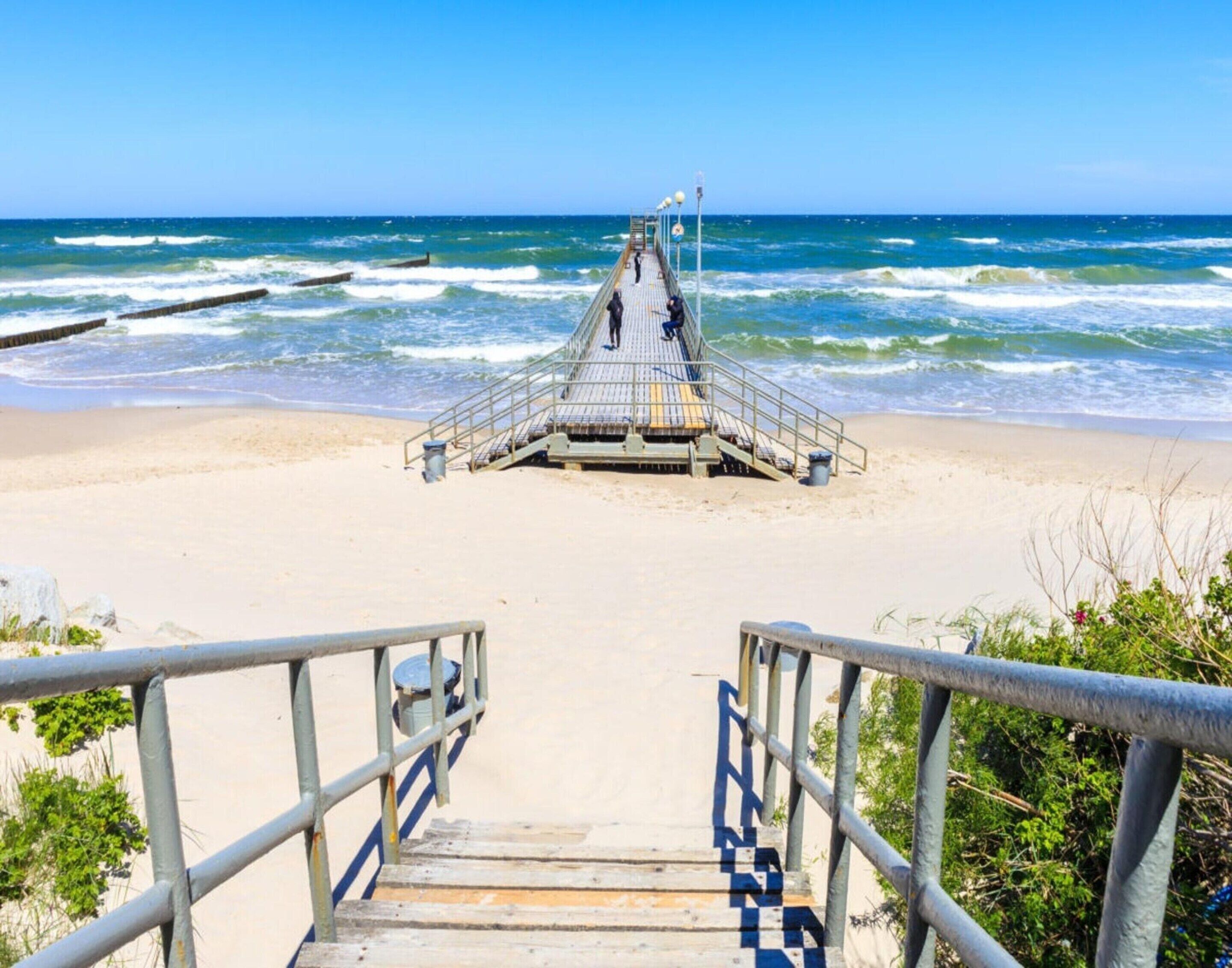 Une promenade en bois menant à un poste de surveillance des sauveteurs sur une plage, avec des vagues en arrière-plan.