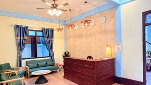 Ein Empfangsbereich mit einem Holztresen, grünen Sitzmöglichkeiten und einem Deckenventilator.