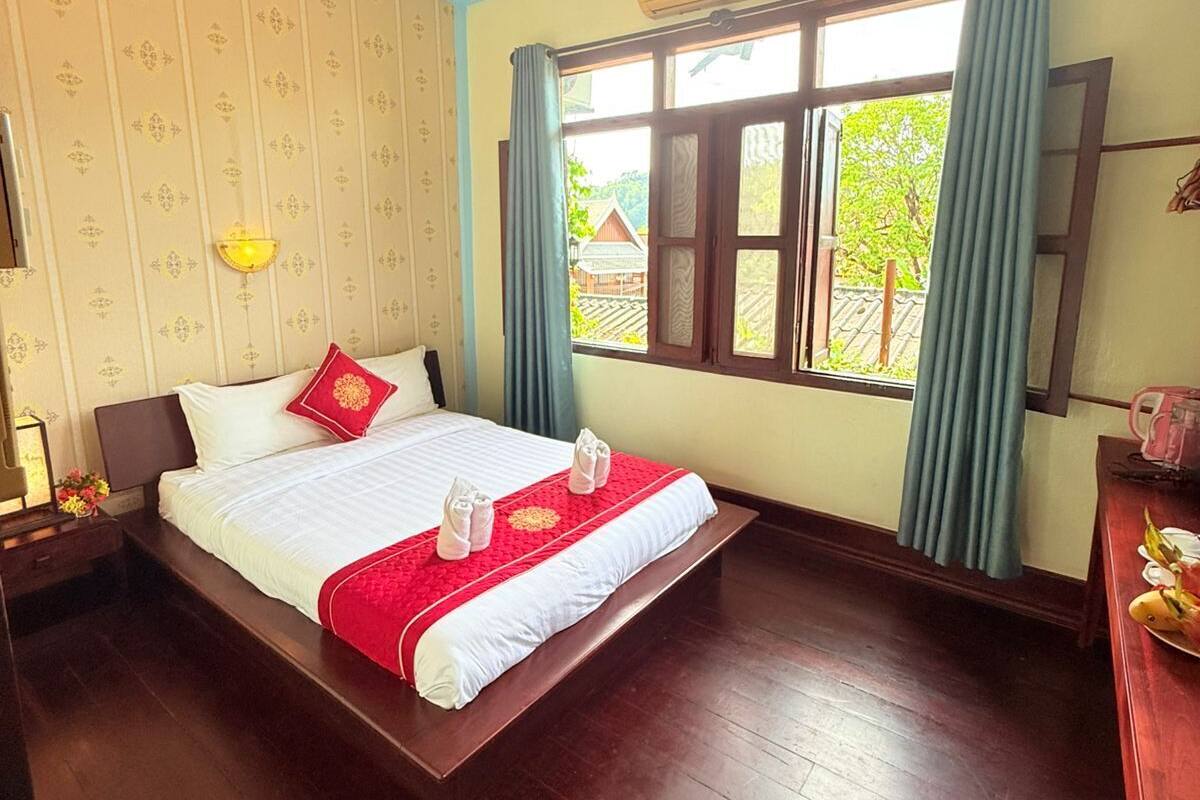 A hotel room with a large bed, a ceiling fan, a window with curtains, and a wooden floor.