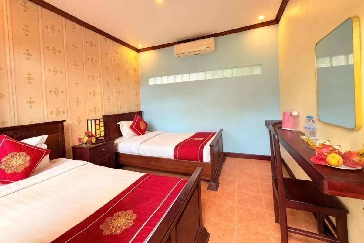 A hotel room with two beds, a desk, a mirror, and an air conditioning unit.