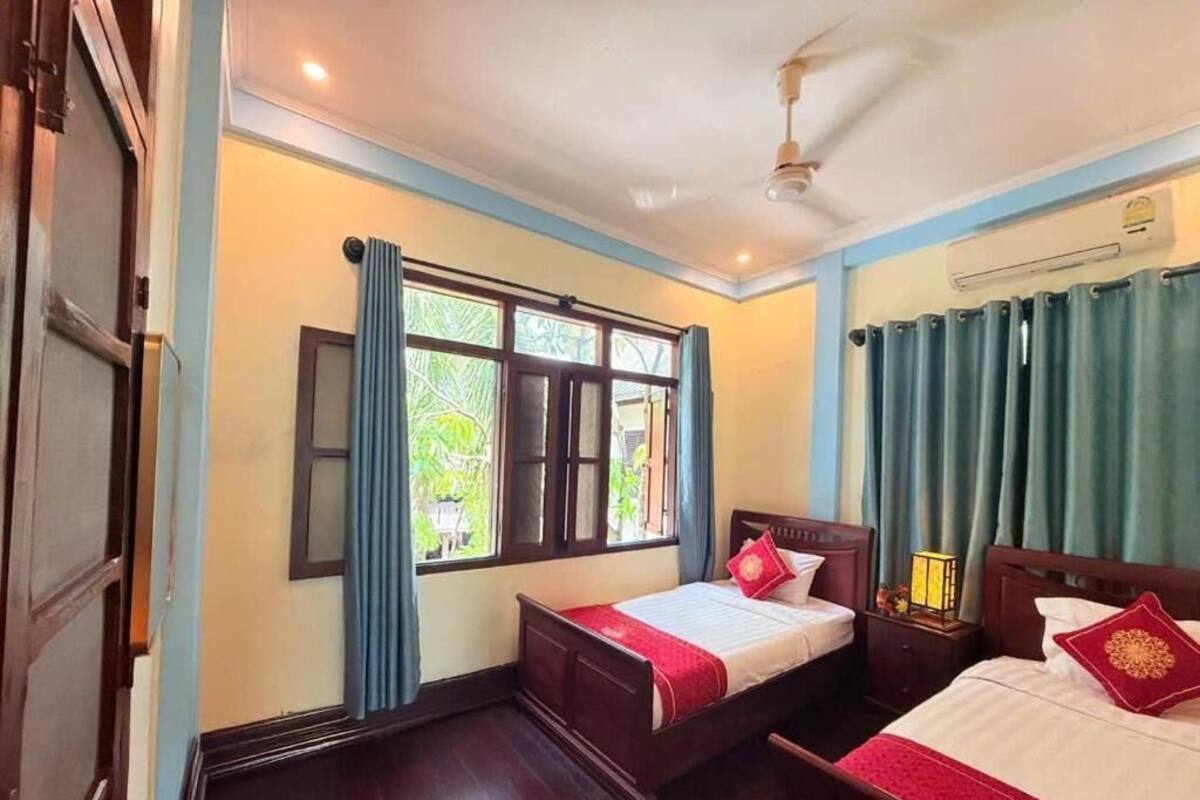 A room with two beds, a ceiling fan, and a window with curtains.