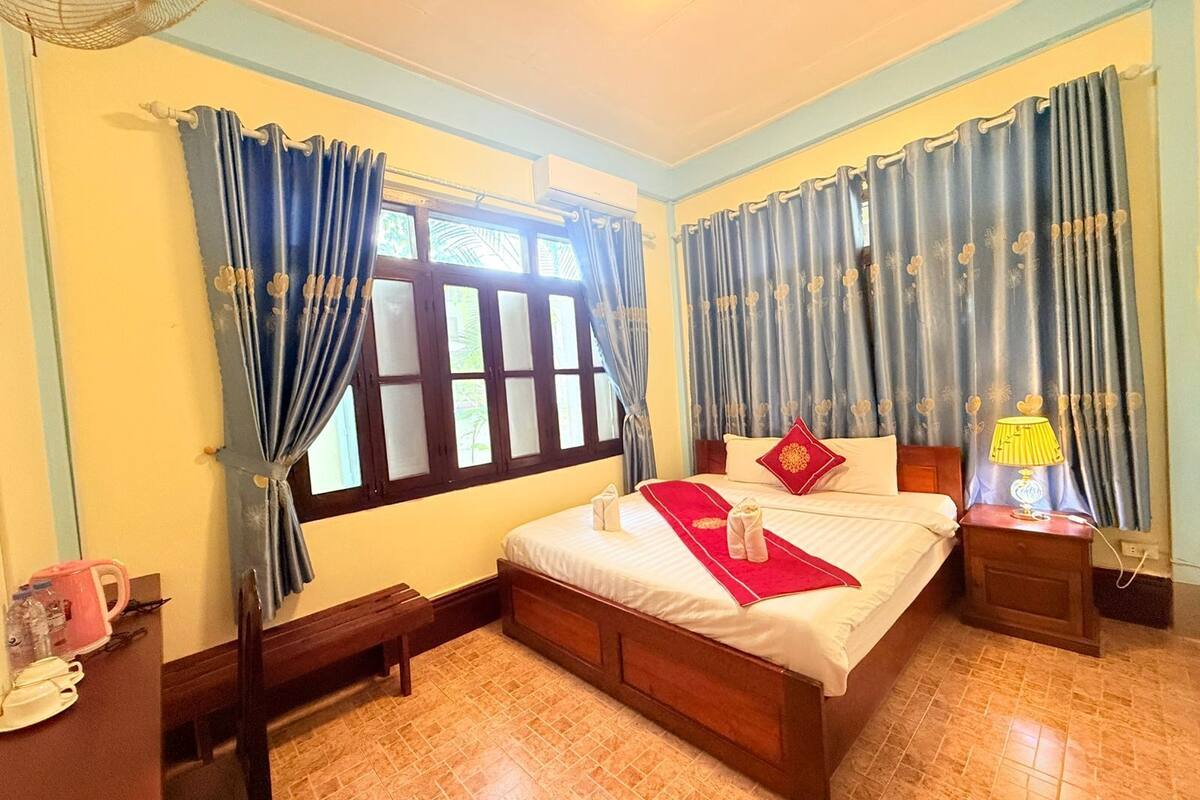 A bedroom with a bed, curtains, a bedside table, a lamp, and a window.