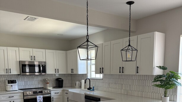A modern kitchen with white cabinetry, a central island, stainless steel appliances, and pendant lighting. - Charming 3-bedroom house in enchanting St. Augustine with AC (St. Augustine)