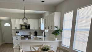 A modern kitchen with white cabinets, a wooden dining table, and a potted plant. - Charming 3-bedroom house in enchanting St. Augustine with AC (St. Augustine)