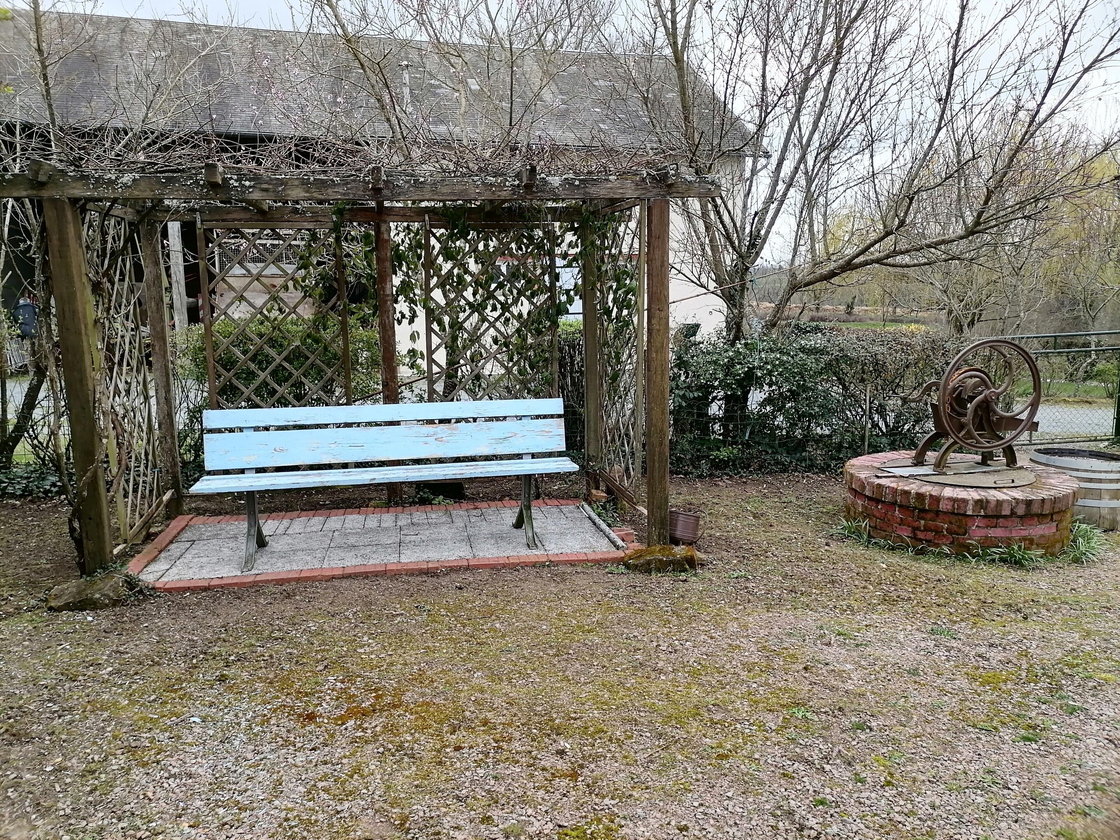 Un porxo de fusta amb una banca, envoltat d'un camí de grava i vegetació.