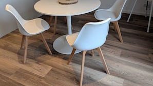 A round table with a vase of pampas grass, surrounded by four white chairs with wooden legs.