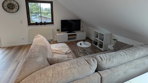 A modern loft-style living room with a large sectional sofa, a flat-screen TV, and a dining area.