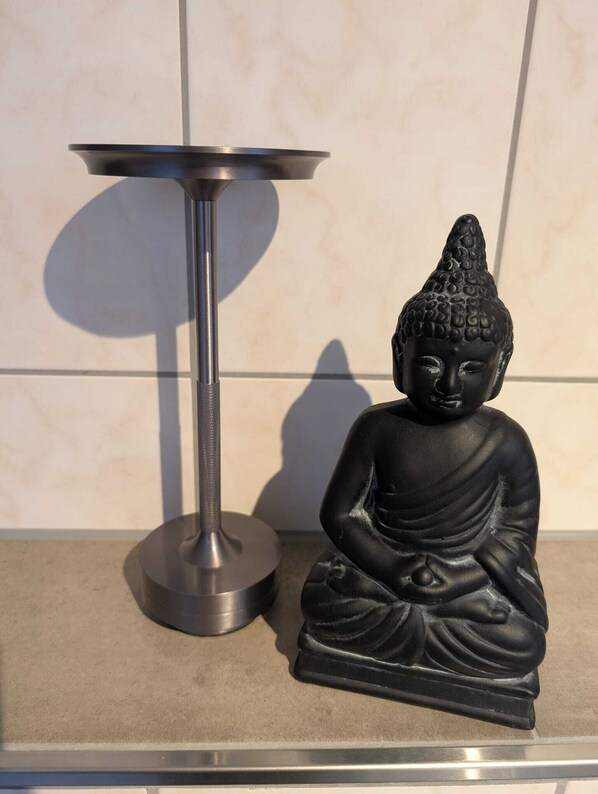 A black Buddha statue next to a metallic table. - Egge Träume - Vacation Apartment in the Teutoburg Forest (Schlangen)