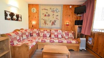 A cozy room with a wooden sofa, a wooden bench, a wall clock, a television, and a radiator.