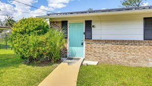 Une maison de plain-pied avec une porte bleu clair, une façade en briques et un petit jardin devant, avec un chemin menant à la porte.