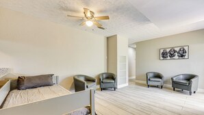 Une chambre à coucher avec un lit, deux chaises, un ventilateur de plafond et un tableau accroché au mur.