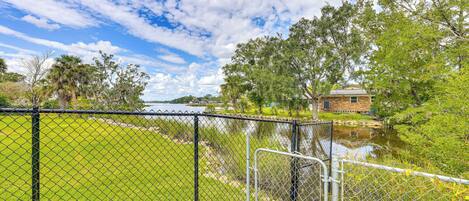 A fenced area with a water body, trees, and a building in the background.