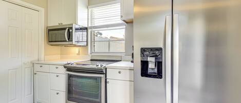 Una cocina con muebles blancos, un refrigerador de acero inoxidable, un microondas, un horno y un dispensador de agua.