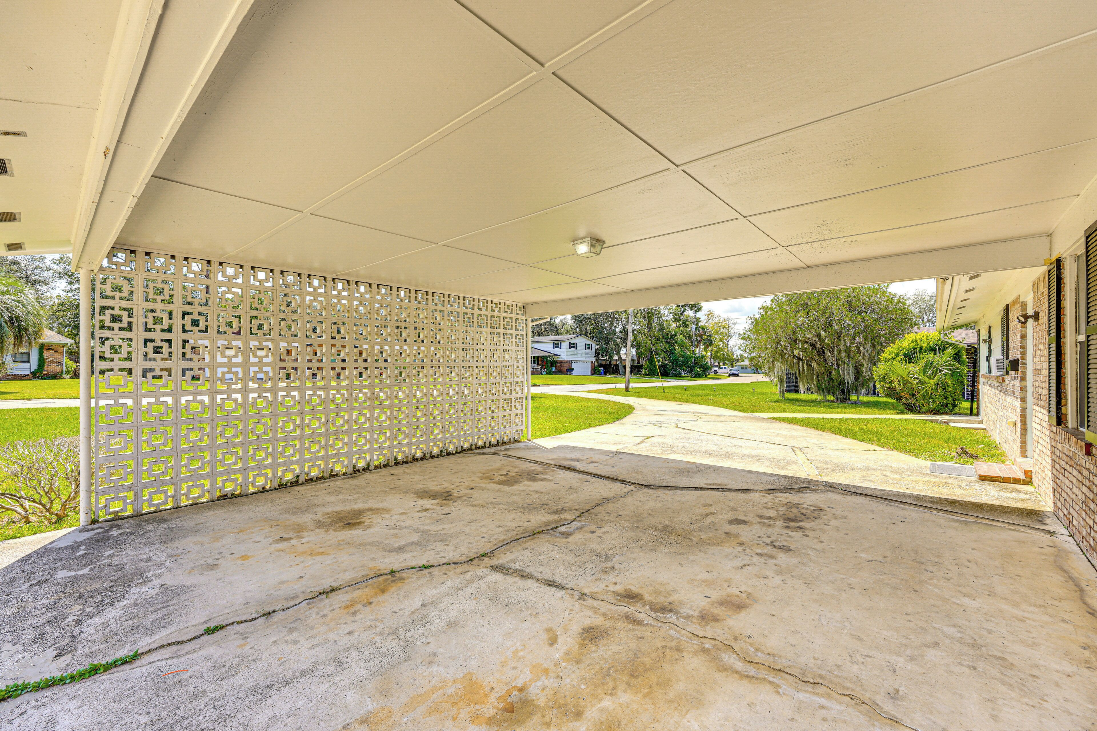 A covered outdoor area with a concrete floor, a decorative lattice fence, and a view of a residential street with houses and greenery.
