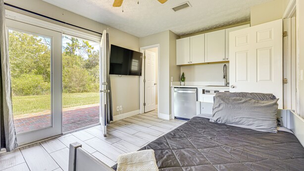 A bedroom with a bed, a ceiling fan, a sliding glass door leading to a patio, and a kitchen area with cabinets and a sink. - Waterfront JAX Townhome w/ River Access! (Jacksonville)