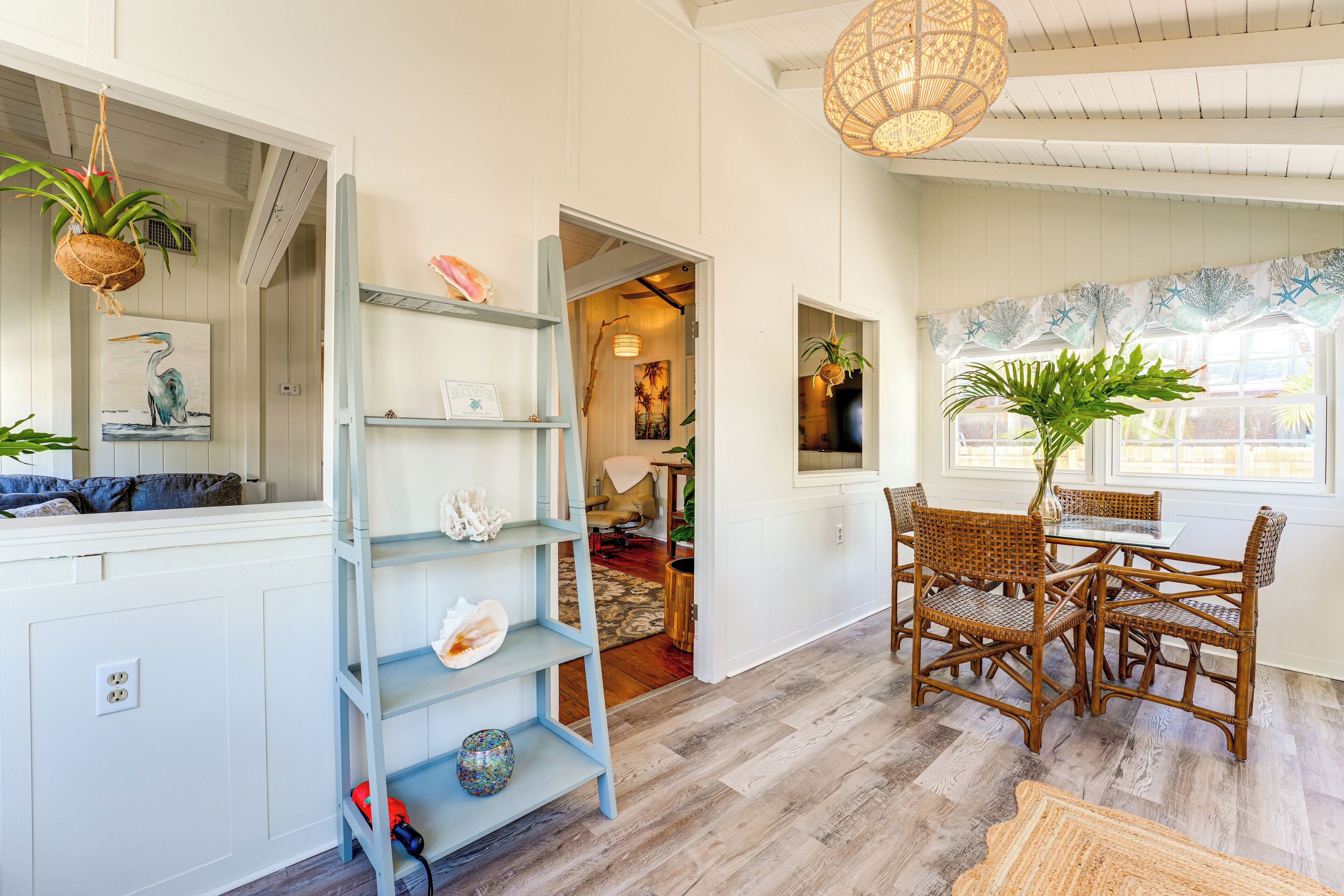 A room with a dining area featuring wicker chairs and a table, a blue shelving unit with decorative items, and a hanging plant.