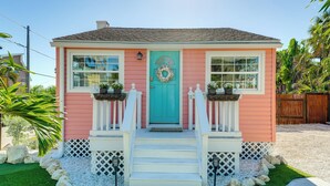 Una casa rosa con una porta turchese, ringhiere bianche e un piccolo portico con gradini.