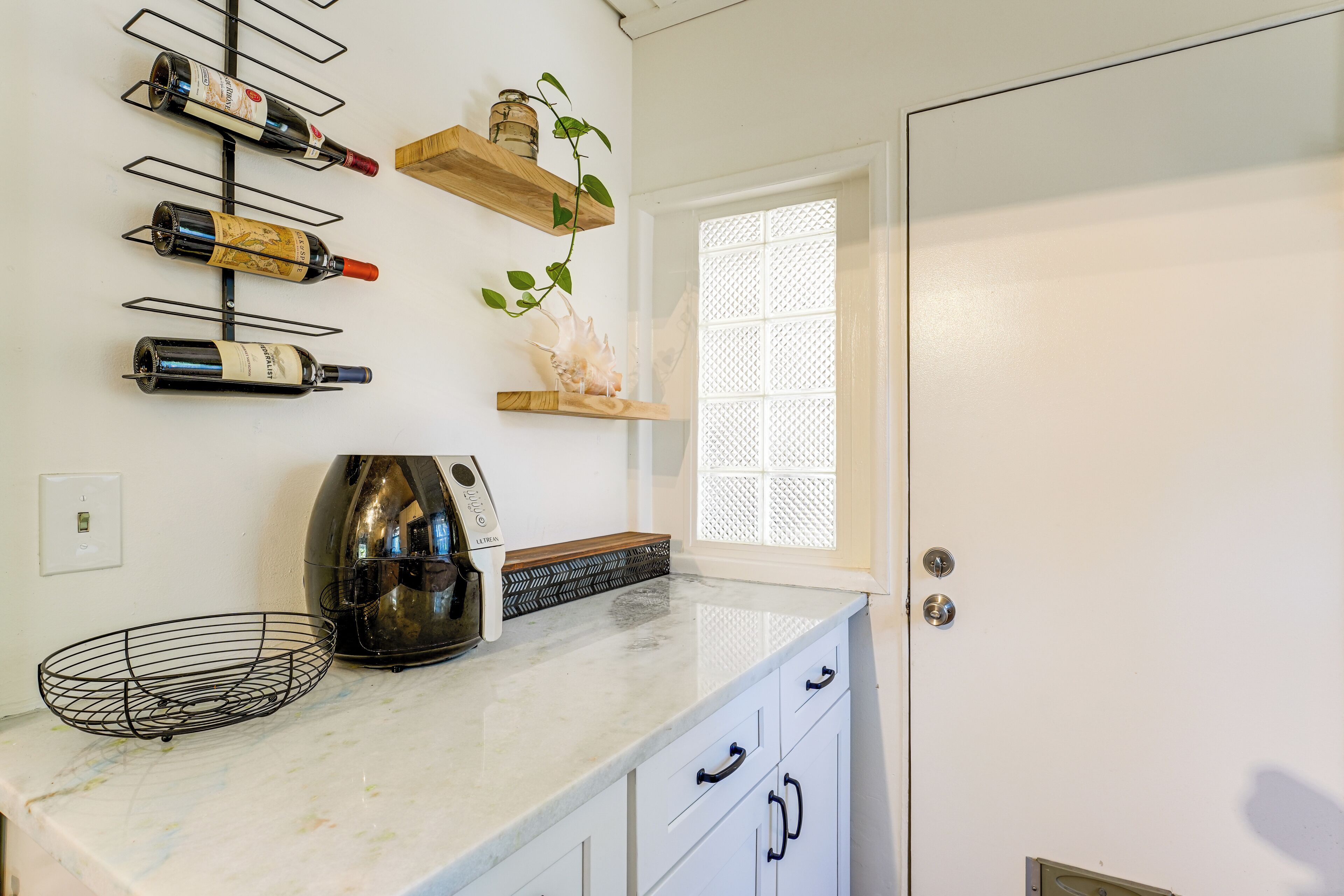 A kitchen with wine bottles on a wall-mounted rack, a coffee maker, and a window with a lattice design.
