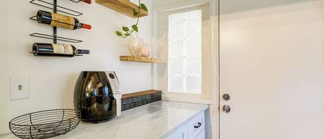 A kitchen with wine bottles on a wall-mounted rack, a coffee maker, and a window with a lattice design.