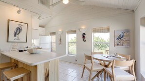 A spacious kitchen with a large island, wooden bar stools, and a dining area with a round table and chairs. - Beachfront Bliss + Bbqs! Indian Rocks Beach Escape (Indian Rocks Beach)