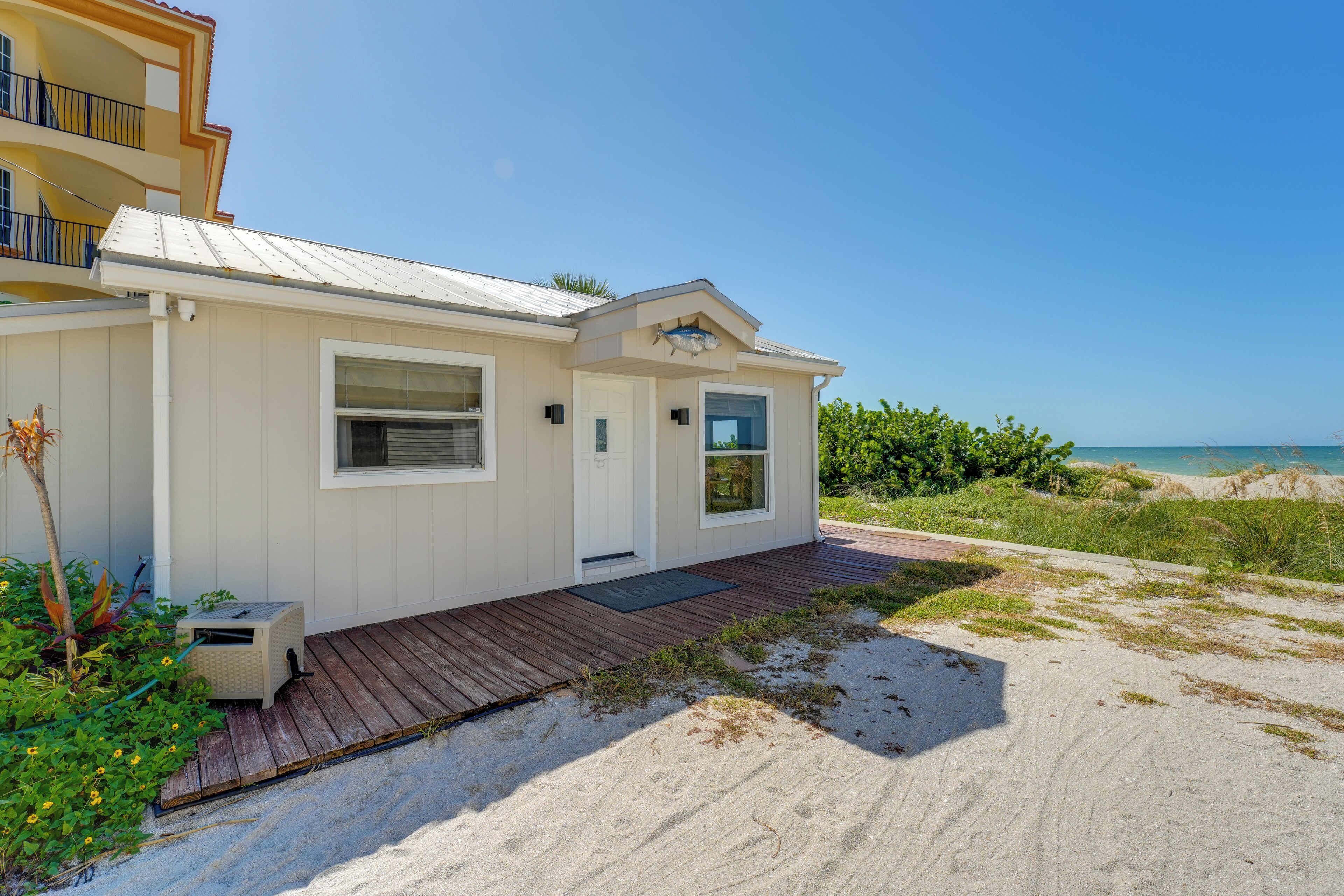 A beachfront house with a wooden deck, a small porch, and a view of the ocean.