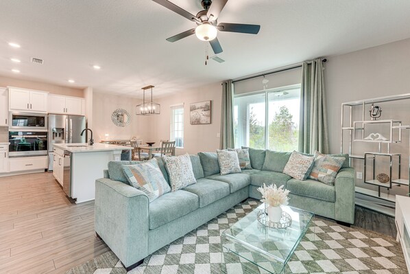 A modern living room with a sectional sofa, a glass coffee table, and a kitchen area with a microwave and refrigerator. - Disney World Group Getaway in Reunion Resort! (Kissimmee)