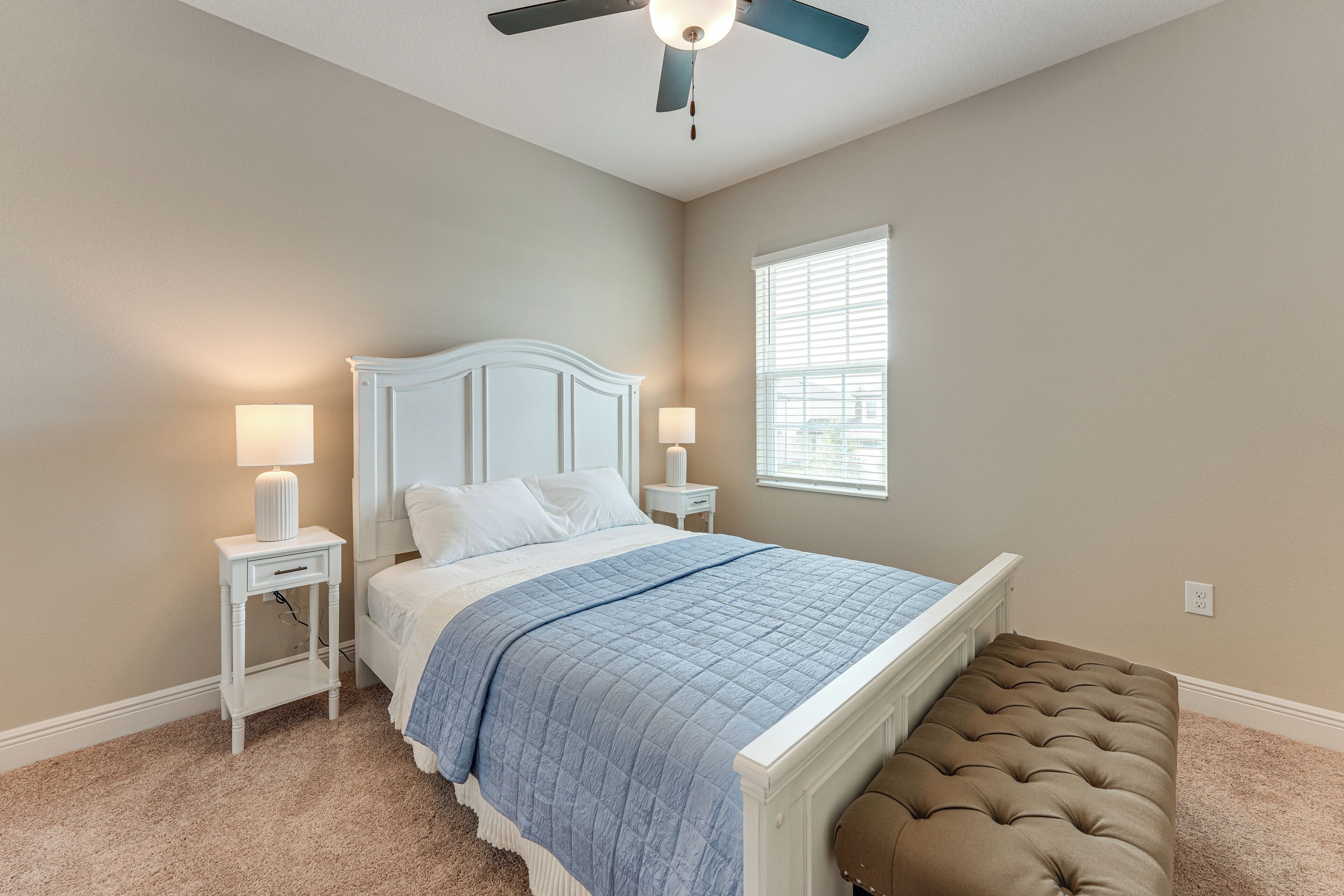 A bedroom with a bed, bedside tables, a ceiling fan, and a window.