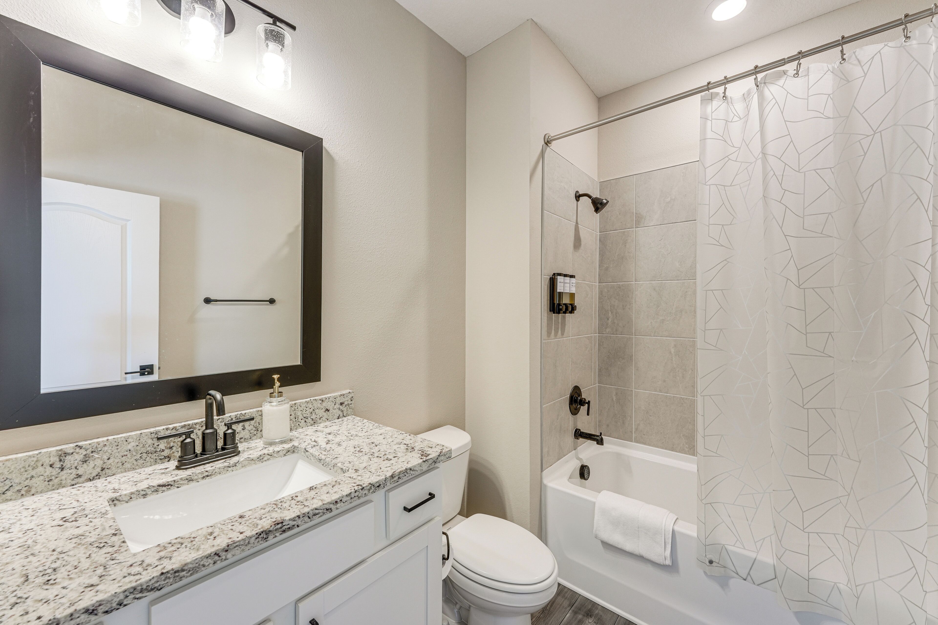 A bathroom with a granite countertop sink, a toilet, a bathtub, and a shower curtain with a geometric pattern.