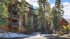 A multi-story building with balconies, surrounded by trees and a snow-covered ground. - Inner Circle Retreat — Walk to Main Street, Pool and the Slopes (Breckenridge)