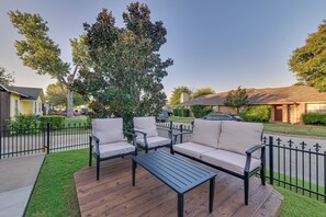 Un patio con terraza de madera, dos sofás beige y una mesa negra.