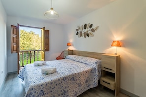 A bedroom with a bed, two bedside lamps, a wooden nightstand, a wall art piece, and a balcony door.