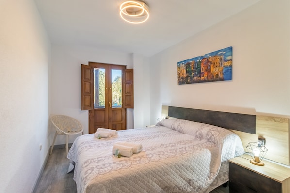 A bedroom with a bed, a chair, a painting, and a nightstand with a lamp.