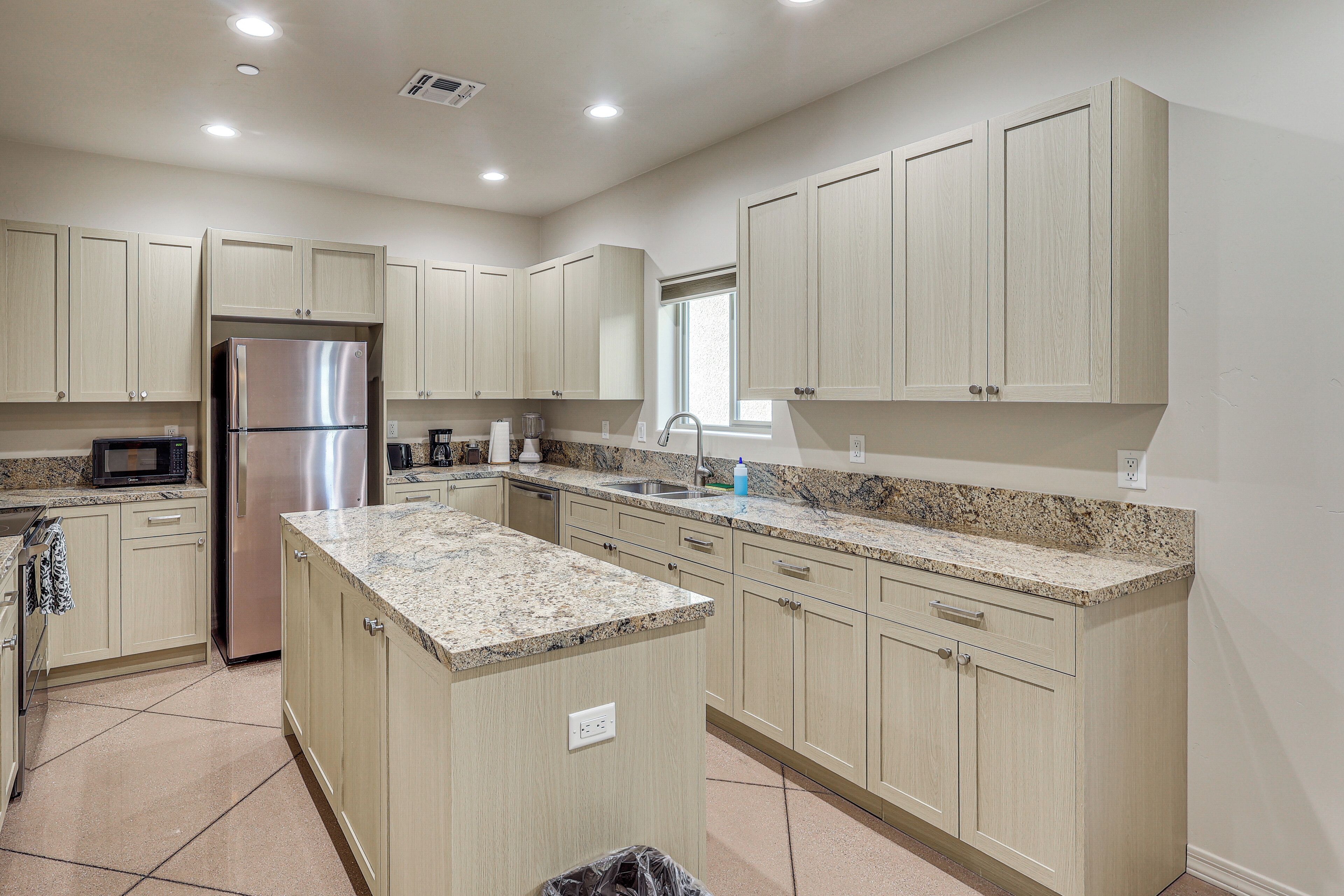A modern kitchen with light wood cabinets, granite countertops, stainless steel appliances, and a large island.