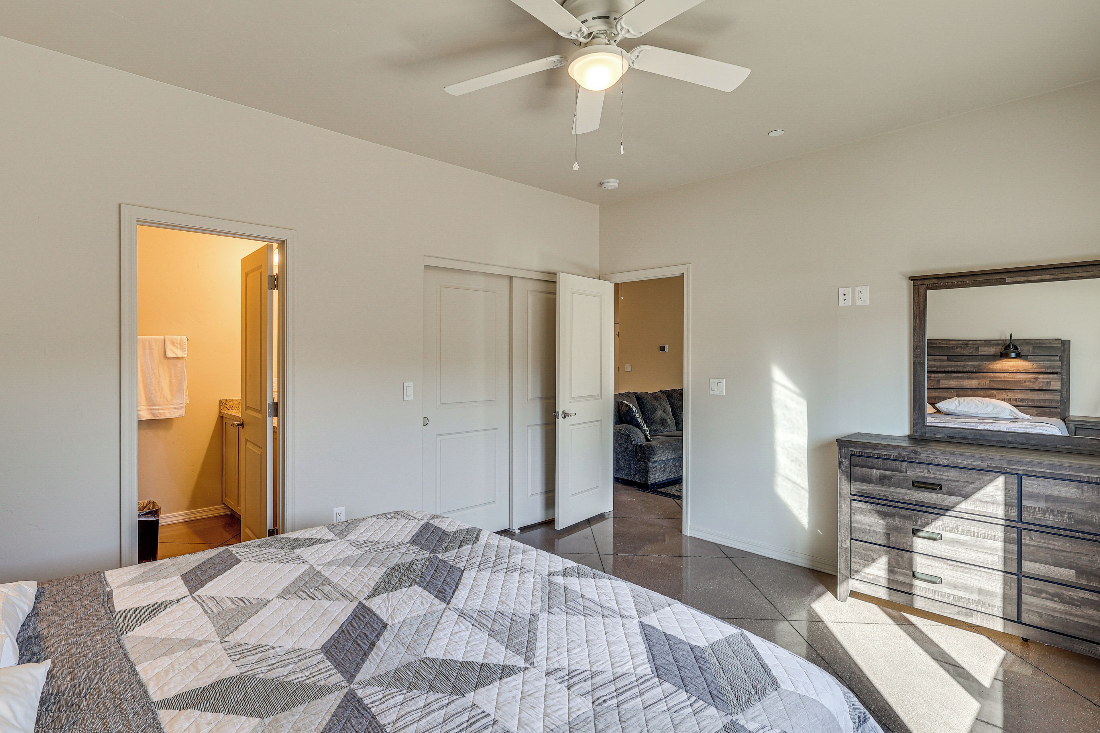 A bedroom with a bed, a dresser, a ceiling fan, and an open door leading to another room.