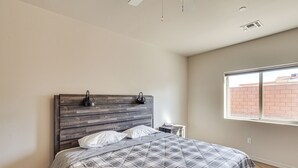 A bedroom with a wooden headboard, a plaid bedspread, a bedside table with a lamp, and a window with a view of a brick building. - Hike & Explore: Apt 3 Mi to Lake Havasu & Dtwn! (Lake Havasu City)