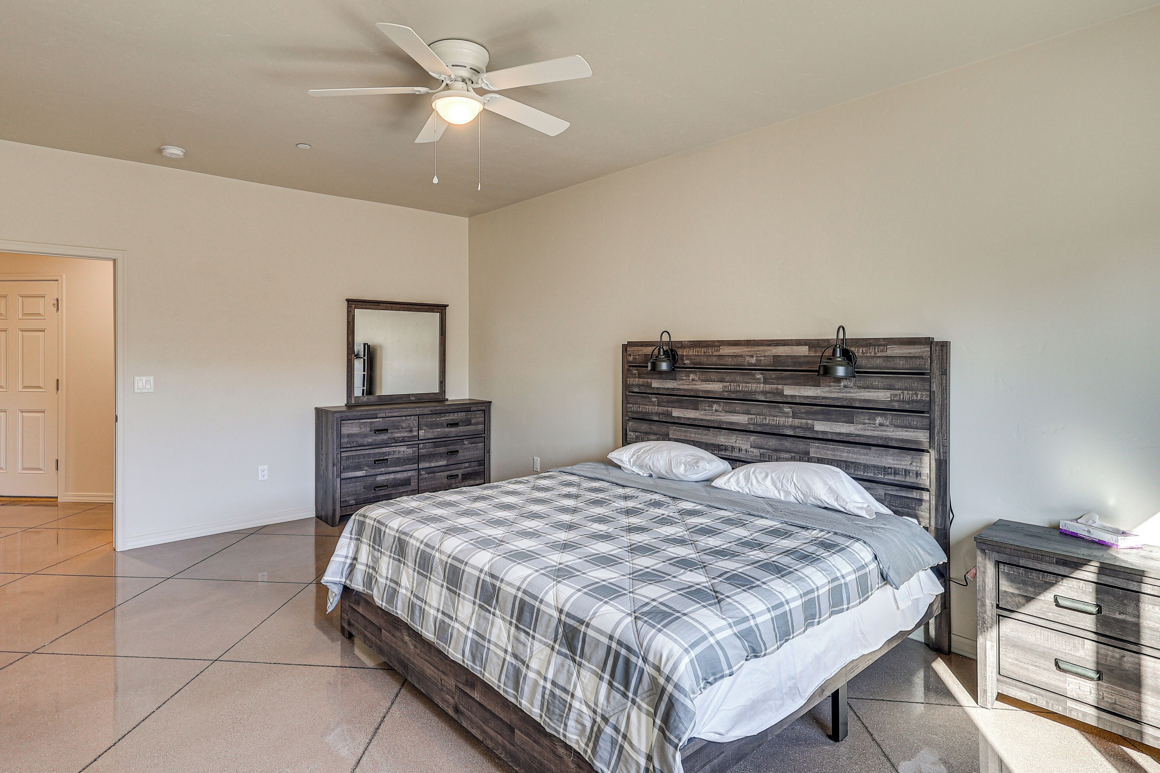 A bedroom with a bed, a dresser, a nightstand, a ceiling fan, and a door.