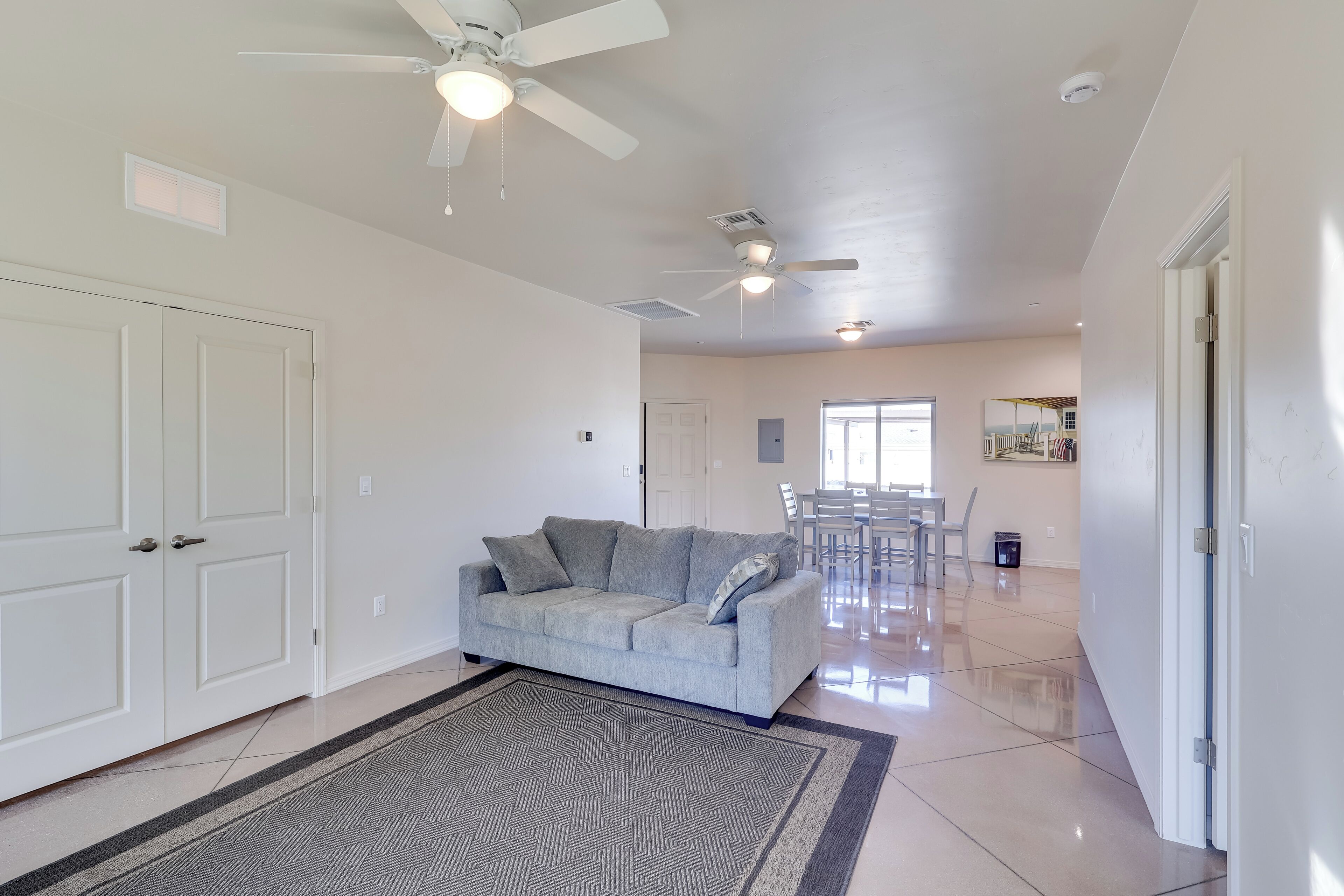 A spacious living area with a grey sofa, white doors, and ceiling fans.