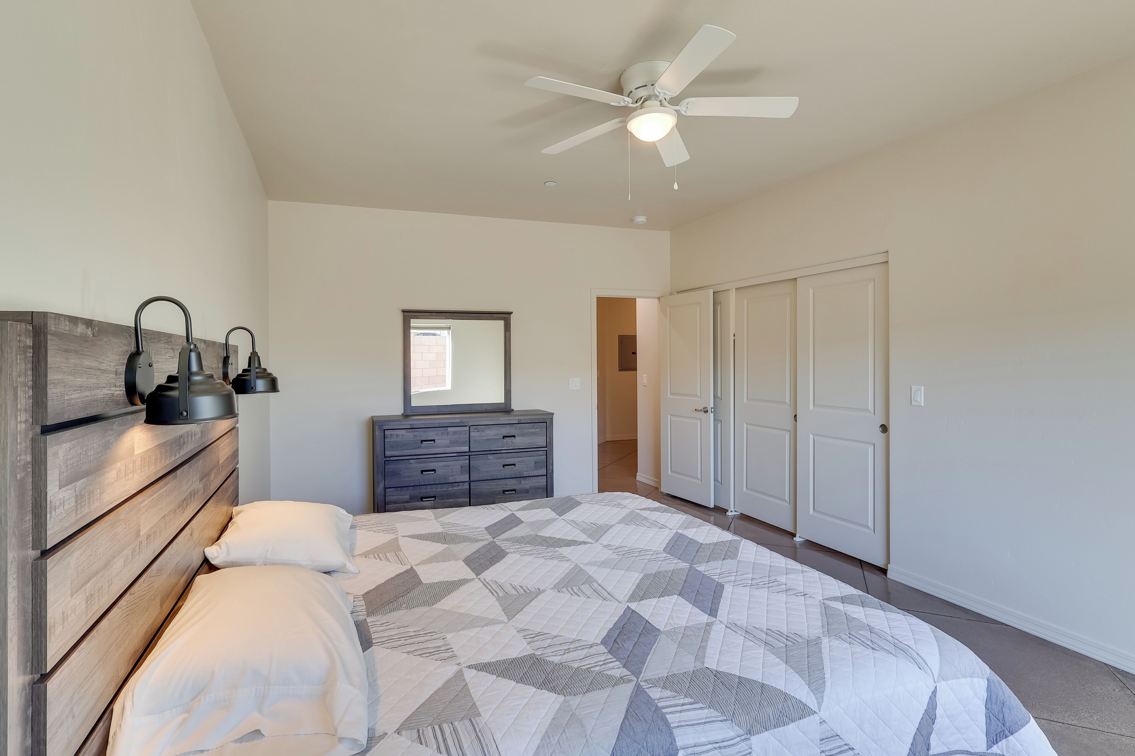 Une chambre à coucher comprenant un lit, une tête de lit en bois, deux lampes de chevet, un ventilateur de plafond, une commode et une armoire.