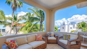 A balcony with wicker furniture, including a sofa and armchairs, with colorful cushions.