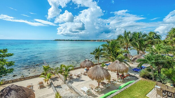 A beach resort with thatched umbrellas, lounge chairs, and a clear view of the ocean and distant buildings.
