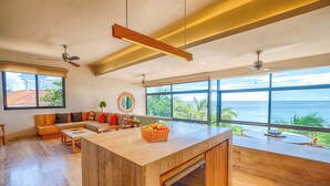 A spacious living area with a large wooden island, a sofa, and a view of the ocean.