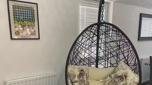 Une pièce comprenant un fauteuil suspendu noir avec des coussins à motifs floraux, une petite table d’appoint noire et un radiateur.