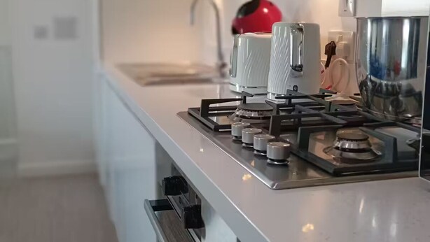 Une cuisine moderne avec une cuisinière en acier inoxydable, des armoires blanches et une bouilloire rouge.