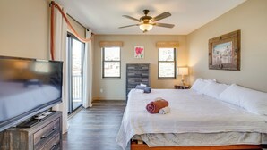 Un dormitorio con cama, televisor, ventilador de techo y ventana con cortinas.