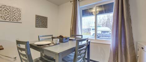 A dining area with a table and chairs, a window with curtains, and decorative wall art.