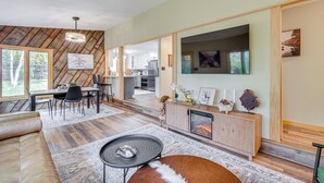 A modern living room with a fireplace, dining area, and kitchen in the background. - 'riverbend Retreat' on 7 Acres w/ River Access! (Webster)